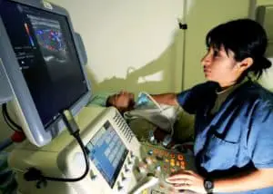 diagnostic medical sonographer salary:: A trained medical progessional earns her ultrasound tech salalry by performing an ultrasound on a patient.